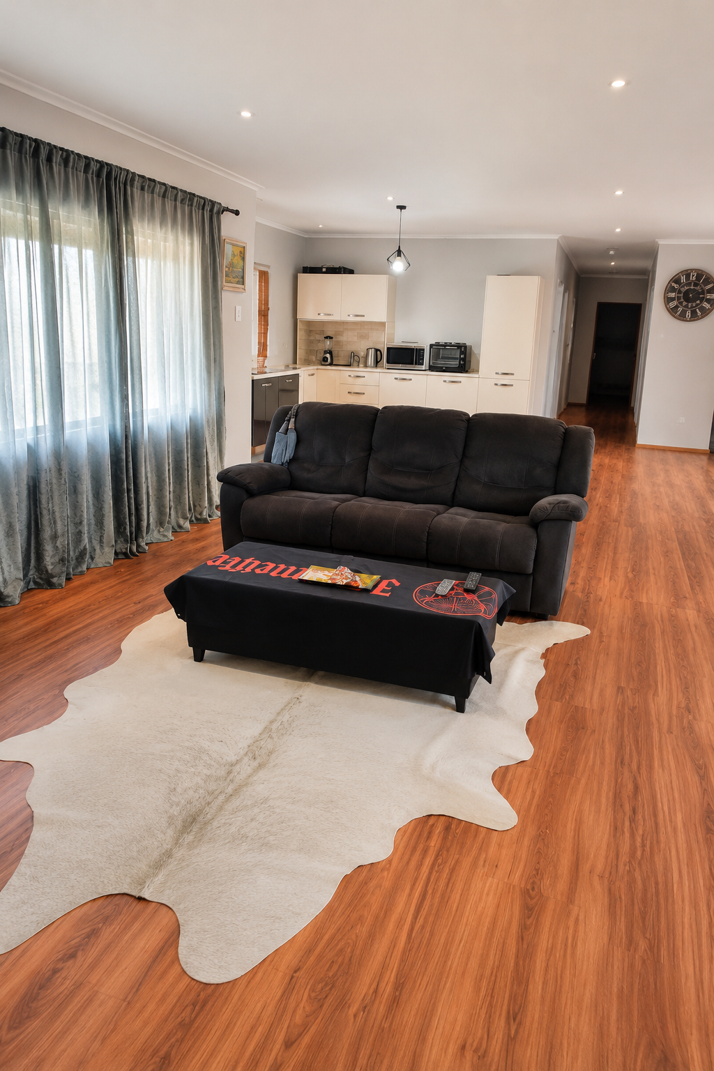 Open-plan lounge with a comfortable sofa, cowhide rug and a kitchen behind